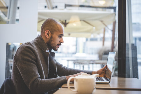 Geschäftsmann sitzt im Café und arbeitet am Laptop - CUF26584