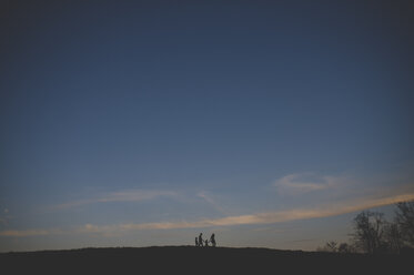 Silhouetted view of parents with son and daughter strolling on hill at dusk - CUF26591