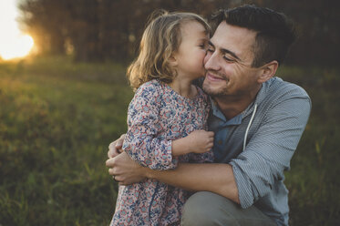 Girl kissing father on cheek in field - CUF26630