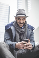 Smiling businessman sitting on stairway reading smartphone text - CUF26641