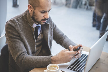 Geschäftsmann sitzt im Café und schreibt eine SMS auf seinem Smartphone - CUF26648