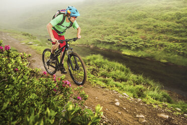 Junger männlicher Mountainbiker, der neben einem Bach radelt - CUF26668