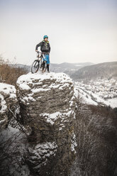 Junger männlicher Mountainbiker auf einer schneebedeckten Felsformation - CUF26675