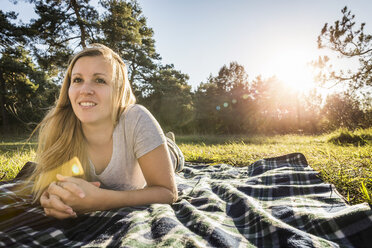 Portrait of young woman lying on picnic blanket in park - CUF26749