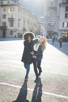 Zwei Freundinnen spazieren und lachen auf dem Stadtplatz - CUF26751
