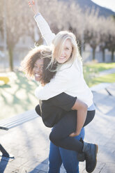 Zwei Freundinnen nehmen sich im Park gegenseitig Huckepack - CUF26754