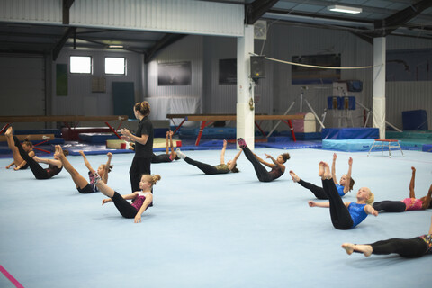 Gymnastiklehrerin beaufsichtigt die Klasse beim Üben von Dehnübungen, lizenzfreies Stockfoto