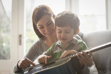 Boy sitting on mother's lap and learning to play guitar - CUF26913