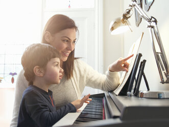 Mother pointing at sheet music to teach son to play piano at home - CUF26915