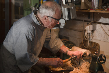 Älterer Mann, der ein Stück Holz mit Tischlerwerkzeugen bearbeitet - CUF26930