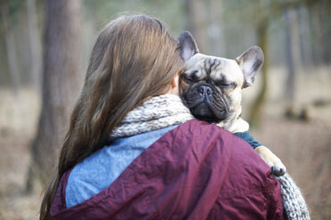 Porträt eines niedlichen Hundes, der von einer jungen Frau durch den Wald getragen wird - CUF26990