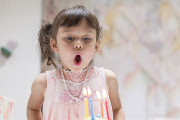 Porträt eines kleinen Mädchens, das brennende Kerzen auf seinem Geburtstagskuchen ausbläst - DRF01741