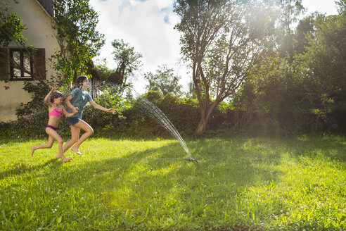 Mädchen und ihre kleine Schwester haben Spaß mit Rasensprenger im Garten - LVF07056