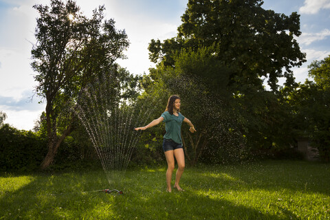 Girl having fun with lawn sprinkler in the garden stock photo