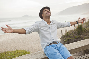 Mid adult man sitting on boardwalk fence with arms open, Rio De Janeiro, Brazil - CUF27101