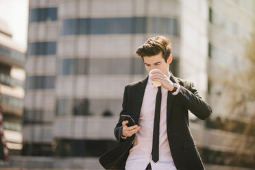 Young businessman drinking take away coffee whilst reading smartphone texts - CUF27113