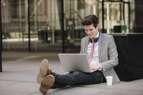 Junger Geschäftsmann auf dem Bürgersteig sitzend mit Laptop, lizenzfreies Stockfoto