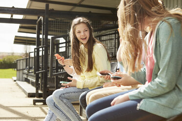 Mädchen und Jungen im Stadion stehen und benutzen Smartphones - CUF27144