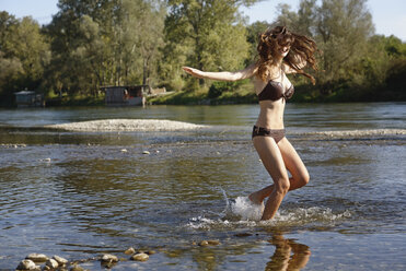 Young woman wearing a bikini splashing and playing in river - CUF27158