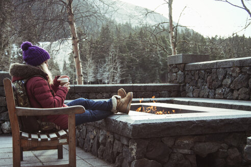 Junge Frau sitzt auf einer Bank mit Feuerstelle, Girdwood, Anchorage, Alaska - CUF27177