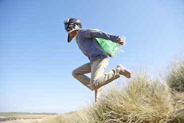 Young boy on beach, wearing fancy dress, pretending to fly - CUF27223