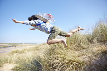 Junger Junge am Strand, der ein ausgefallenes Kleid trägt und in die Luft springt - CUF27225