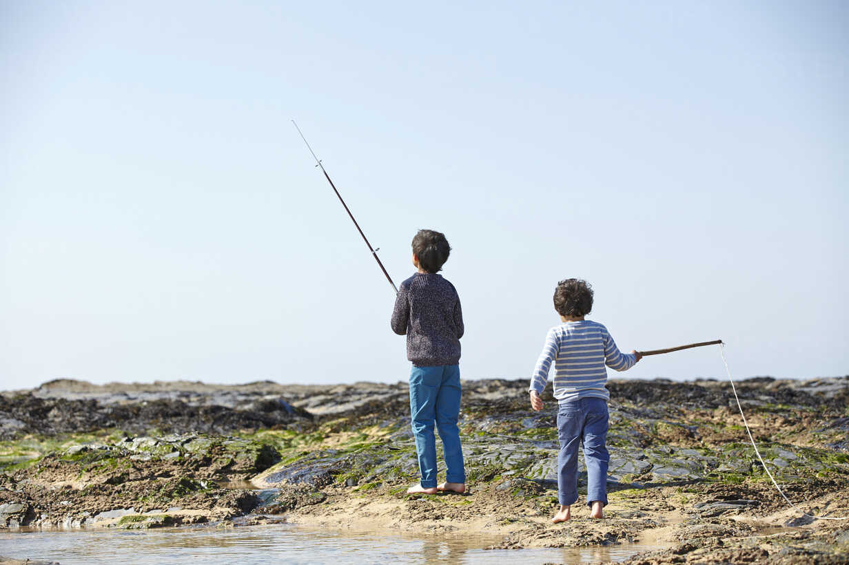 Two young boys, fishing on beach, rear view stock photo