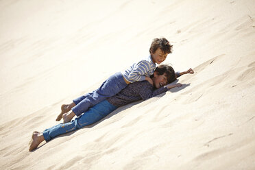 Two young boys lying on sandy hill, playing - CUF27255