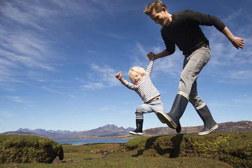 Vater und Sohn halten sich beim Laufen an den Händen, Isle of Skye, Hebriden, Schottland - CUF27297