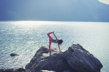 Mittlere erwachsene Frau, die auf einem Felsen am Seeufer balanciert, in Yoga-Position - CUF27327