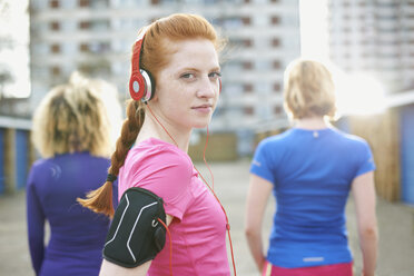 Porträt einer Frau mit Armbinde und Kopfhörern vor dem Sport, die über die Schulter in die Kamera schaut - CUF27359