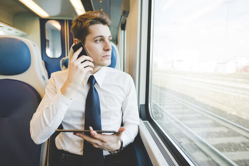 Porträt eines jungen Geschäftsmannes, der im Zug ein digitales Tablet benutzt. - CUF27378