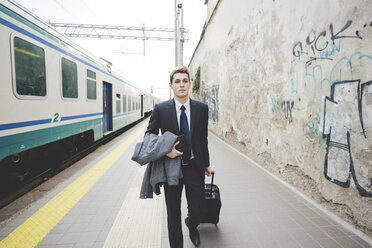 Junger Geschäftsmann, der mit einem Koffer auf dem Bahnsteig spazieren geht. - CUF27379
