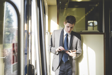 Porträt eines jungen Geschäftsmannes, der im Zug ein digitales Tablet benutzt. - CUF27382