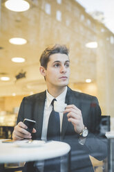 Porträt eines jungen Geschäftsmannes, der in einem Café sitzt und ein digitales Tablet und ein Mobiltelefon benutzt. - CUF27388