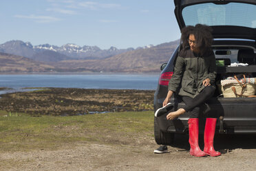 Mittlere erwachsene Frau sitzt auf einem Kofferraum und zieht Schuhe an, Loch Eishort, Isle of Skye, Hebriden, Schottland - CUF27392