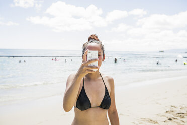 Junge Frau im Bikini-Oberteil macht ein Smartphone-Selfie am Waikiki Beach, Hawaii, USA - CUF27440