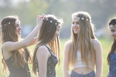 Teenager-Mädchen, die im Park Kopfbedeckungen aus Gänseblümchenketten aufsetzen und tragen, lizenzfreies Stockfoto