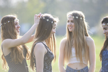 Teenager-Mädchen, die im Park Kopfbedeckungen aus Gänseblümchenketten aufsetzen und tragen - CUF27469