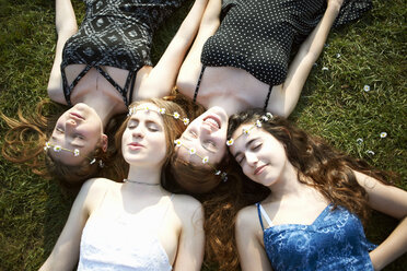 Vier Teenager-Mädchen mit Gänseblümchen-Kopfschmuck liegen auf dem Rasen eines Parks - CUF27470