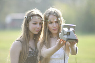 Zwei Teenager-Mädchen im Park machen ein Selfie mit einer Sofortbildkamera - CUF27472