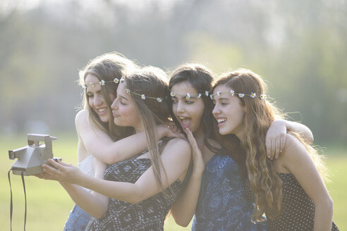 Vier Teenager-Mädchen im Park machen ein Selfie mit einer Sofortbildkamera - CUF27473