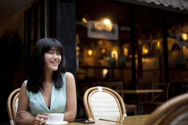 Junge Frau, die vor einem Café sitzt und Kaffee trinkt, Shanghai, China - CUF27501