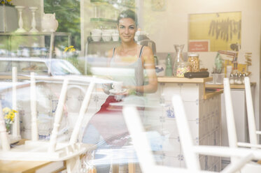 Junge Kellnerin sitzt in einem Café, Blick durch ein Fenster - CUF27510