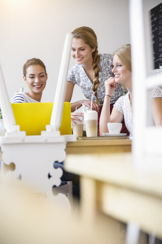 Junge Frauen lächelnd mit Blick auf Laptop, lizenzfreies Stockfoto