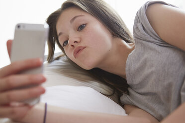 Girl lying on bed peering at smartphone text message - CUF27552