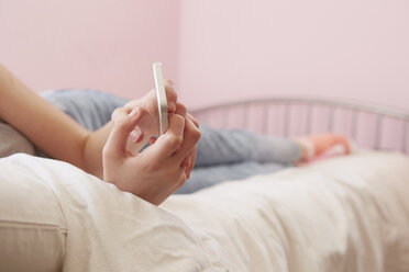 Abgeschnittene Ansicht eines Mädchens, das auf dem Bett liegt und eine Smartphone-Textnachricht liest - CUF27554