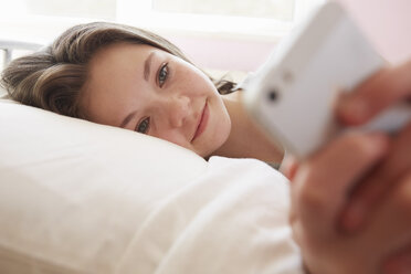Mädchen liegt auf dem Bett und schreibt eine SMS auf dem Smartphone - CUF27555
