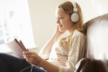 Girl on sofa wearing headphones listening to music from digital tablet - CUF27561