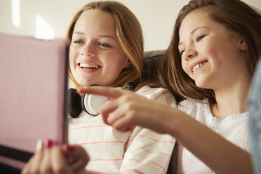 Two girls on sofa laughing and pointing at digital tablet - CUF27563